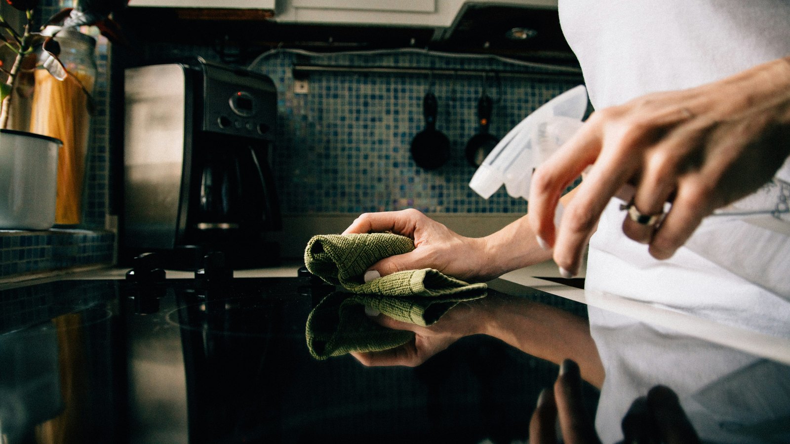 Hands wiping down a kitchen counter with a cloth and spray